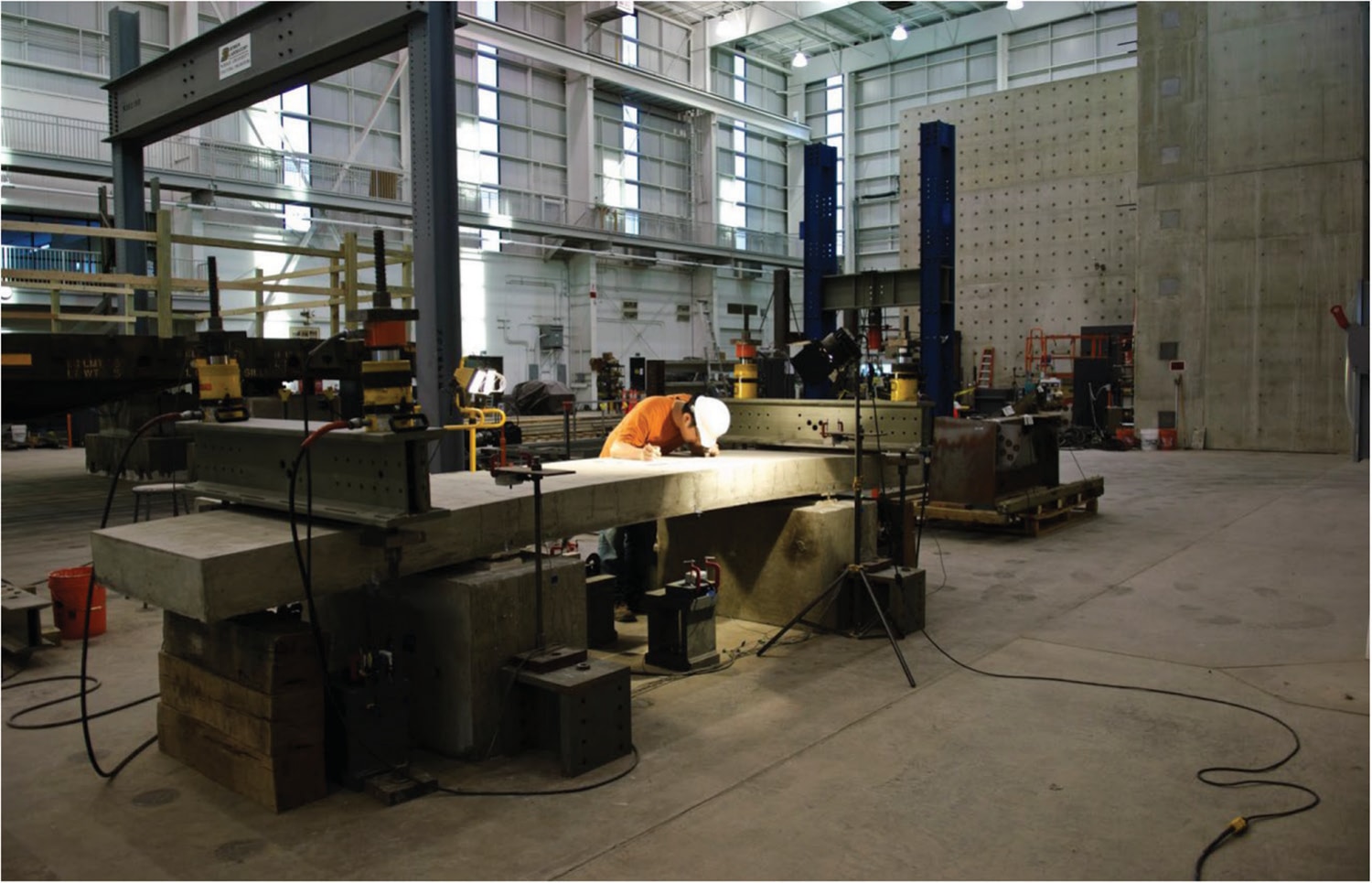 Chungwook Sim wearing a hard hat and examining a concrete slab during structural testing in a laboratory.